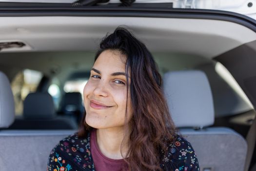 Close-up of beautiful brunette woman smiling in the back of SUV. Portrait of happy woman with wavy hair and the interior of a vehicle as background. People and transportation