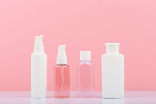 Set of cosmetic products for skin cleaning, exfoliating and moisturizing. Cosmetic bottles against pink background. Concept of skin care and beauty