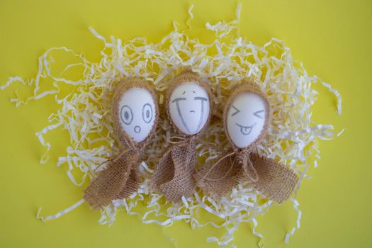 White eggs with funny faces in sackcloth on a yellow background. Easter Concept.