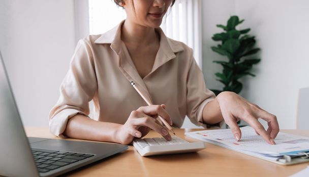 Close up of businesswoman or accountant hand holding pencil working on calculator to calculate financial data report, accountancy document and laptop computer at office, business concept