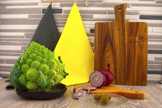 Salad preparation. Cauliflower romanesco, red onion and olives prepared for salads on the kitchen table, against the background of multicolored cloths