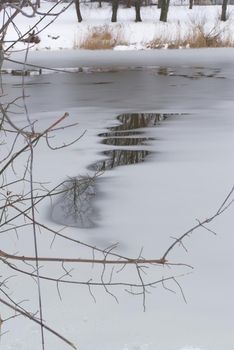 Thawing water in a frozen pond or lake in early spring collecting on the surface of the ice with reflections of the surrounding trees in a concept of the seasons