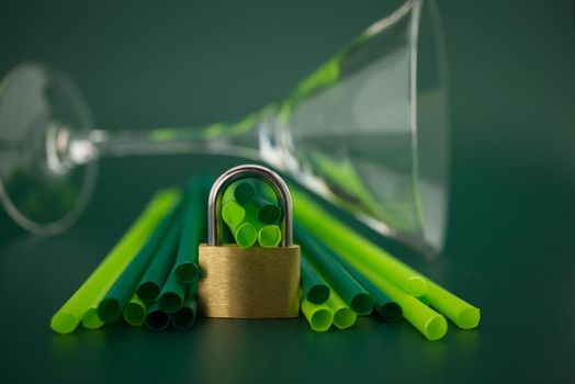Golden padlock in front of plastic drink straws on a green background. Phase out plastic drinking straws concept