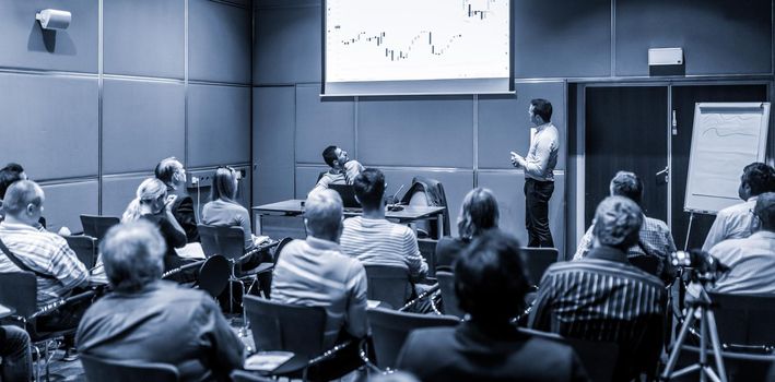 Speaker giving a talk in conference hall at business event. Unrecognizable people in audience at conference hall. Business and Entrepreneurship concept. Blue toned black and white.