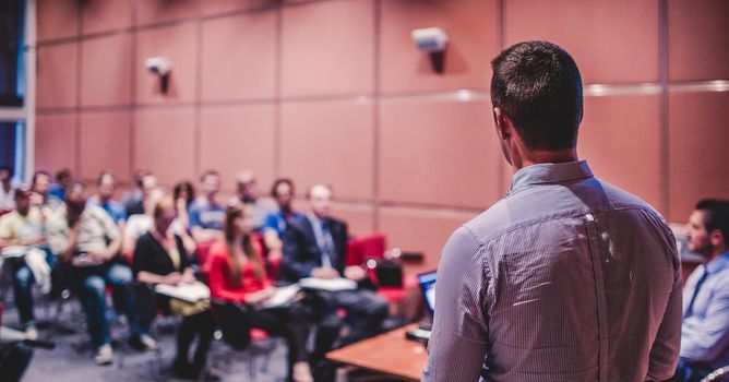 Speaker giving a talk on corporate business conference. Unrecognizable people in audience at conference hall. Business and Entrepreneurship event.