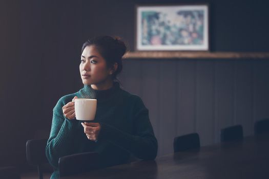 Asian woman drinking coffee beside window in winter color tone