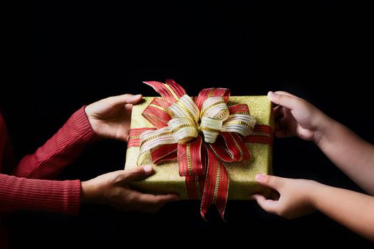 Hands of parent giving a Christmas gift to child on dark background. Congratulation for child. Photo is take in studio