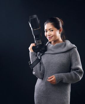 Cheerful female photographer using DSLR camera working on studio