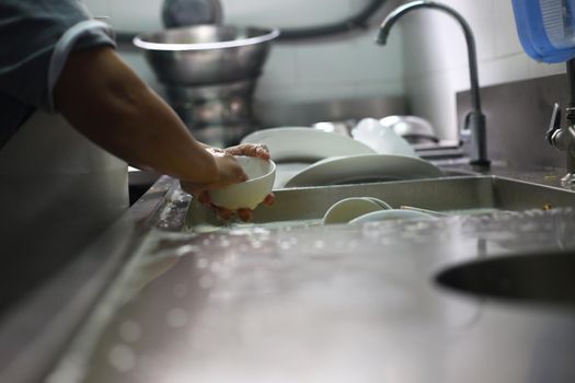 Man washing dish on sink at restaurant