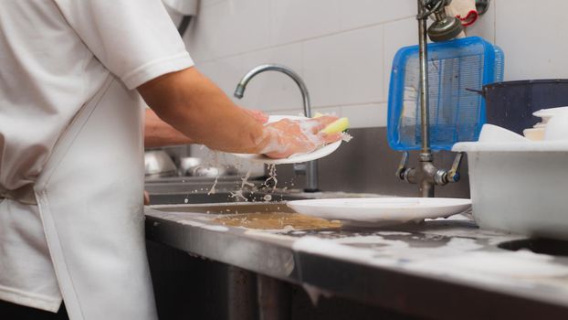 Man washing dish on sink at restaurant