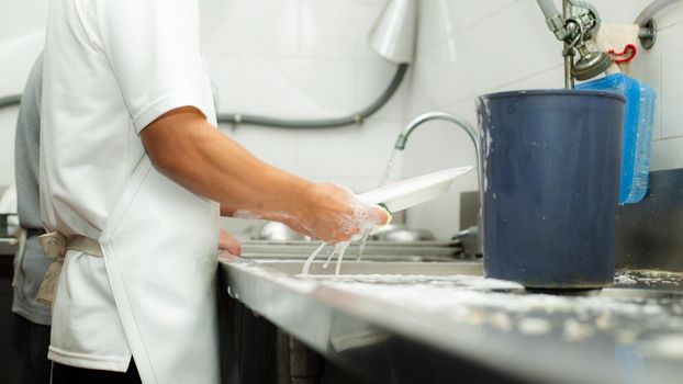 Man washing dish on sink at restaurant