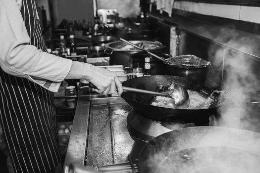 Chef stir fry busy cooking in kitchen. Black and white filter