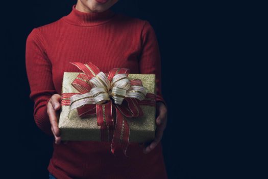 Young woman hands holding gold gift box on dark background