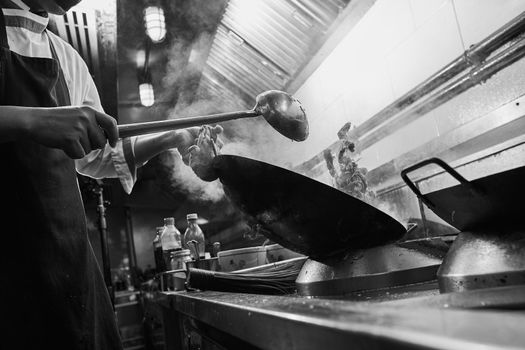 Chef stir fry cooking in kitchen. Black and white filter