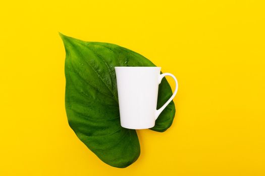 White coffee cup resting on a green leaf and a yellow background. minimalist photo style