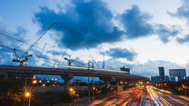 Busy traffic in the city late at night with cranes working,
Picture with the electric car Car light Skies with clouds and big cities