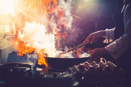 Chef stir fry busy cooking in kitchen. Chef stir fry the food in a frying pan, smoke and splatter the sauce in the kitchen.