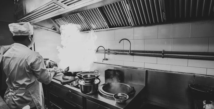 Chef stir fry busy cooking in kitchen. Chef stir fry the food in a frying pan, smoke and splatter the sauce in the kitchen. monochrome filter