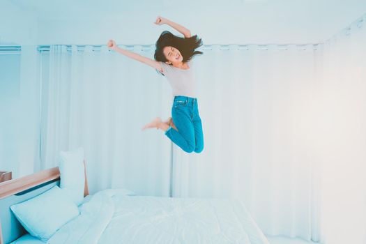 Asian woman jumping on her bed with extreme joy after canceling the anti-virus Covid-19 measures.