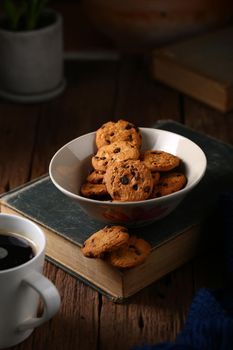 Still life with chocolate chip cookies in cup bowl on old book