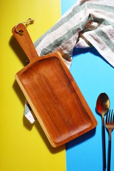 Empty wooden tray placed with spoon on a colorful background