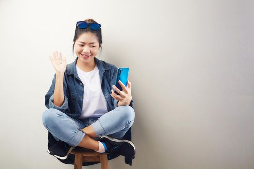 Smiling young Asian woman making video call on smartphone over gray background