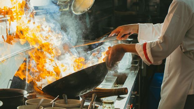 Chef stir fry busy cooking in kitchen. Chef stir fry the food in a frying pan, smoke and splatter the sauce in the kitchen.