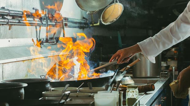 Chef stir fry busy cooking in kitchen. Chef stir fry the food in a frying pan, smoke and splatter the sauce in the kitchen.