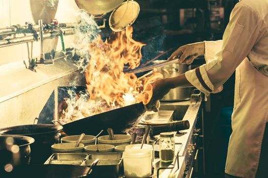 Chef stir fry busy cooking in kitchen. Chef stir fry the food in a frying pan, smoke and splatter the sauce in the kitchen.