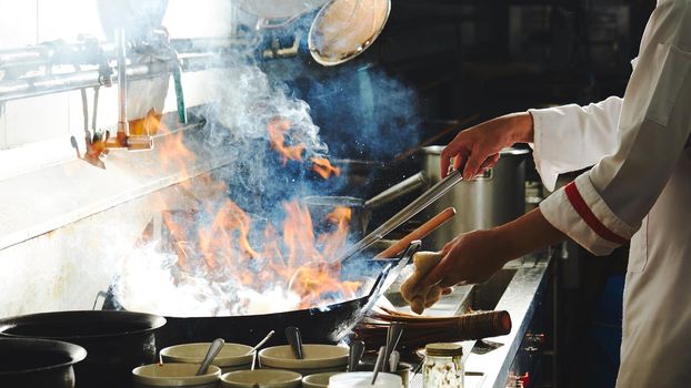 Chef stir fry busy cooking in kitchen. Chef stir fry the food in a frying pan, smoke and splatter the sauce in the kitchen.