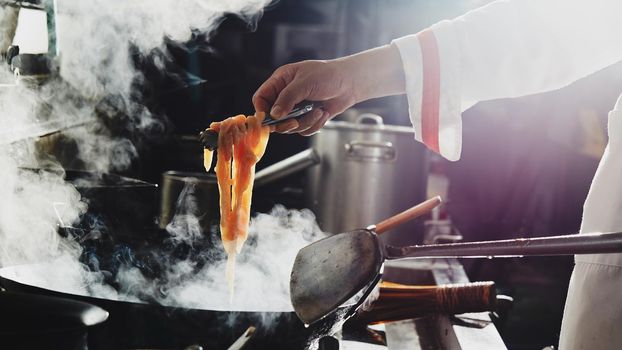 Chef stir fry busy cooking in kitchen. Chef stir fry the food in a frying pan, smoke and splatter the sauce in the kitchen.