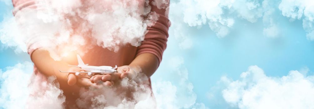 Woman's hand flying toy plane with clouds on blue sky background