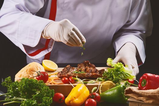 Gloved chef decorating the steak by sprinkling parsley.