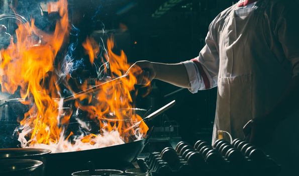 Chef stir fry busy cooking in kitchen. Chef stir fry the food in a frying pan, smoke and splatter the sauce in the kitchen.