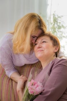 A young girl congratulates her mother on the holiday. Hugs gently and smiles.