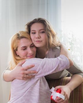 A young girl congratulates her mother on the holiday. Hugs gently and smiles.