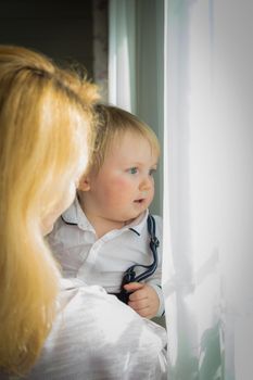 Mom hugs and kisses the baby standing by the window. Mother's day holiday