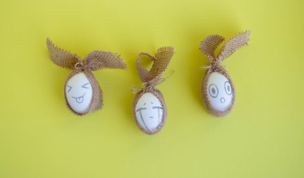 White eggs with funny faces in sackcloth on a yellow background. Easter Concept.