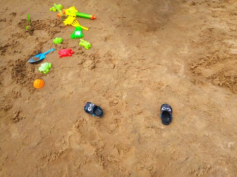 Concept of beach recreation for children. Bright plastic children's toys in the sand. Top view. Space for text.