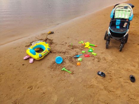 The concept of a beach holiday for children. Baby stroller and bright plastic children's toys in the sand. Space for text.