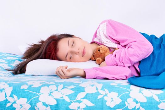 Close up of a beautiful young girl in pink pajamas sleeping calmly in her bed, hugging a cute plush teddy bear. Sleep and relaxation concept.