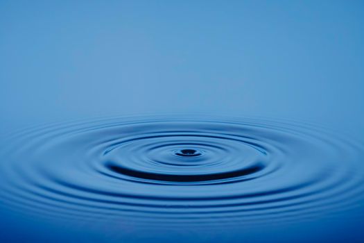 Closeup Water drop or splash falling on the surface of the water and beautiful circular wave ripple, water concept, with blue background