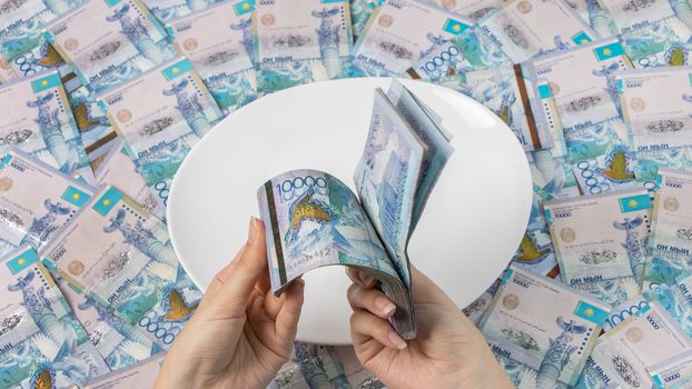 Count money in tenge. A lot of Kazakhstani tenge on a white plate. The national currency of Kazakhstan. Salary in tenge. To cut the budget.
