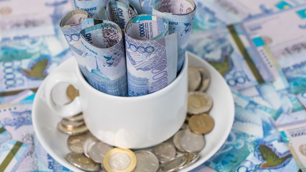 Kazakhstani tenge in a mug on a plate on the table. The national currency of Kazakhstan. Salary in tenge. Grocery basket, budget savings. Divide the budget.