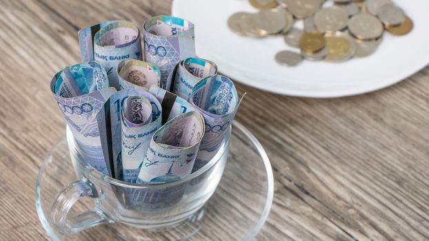 Kazakhstan tenge in a Cup and on a plate on the table.A lot of Kazakh money.Sawing the budget,the subsistence minimum or the dual currency basket in Kazakhstan.The crisis by the fall in exchange rates