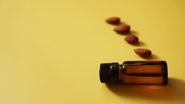 Bottle of almond oil and almonds on yellow background - Bottle and row of nuts