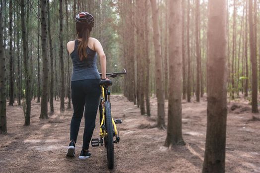 Back young female woman helmet catch bicycle at forest on summer with copy space
