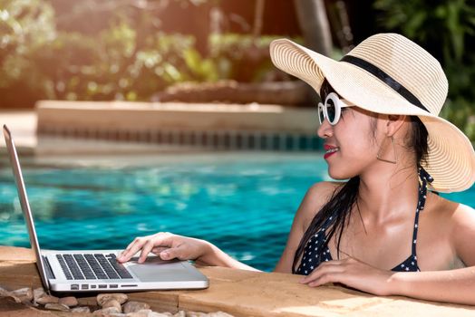 Portrait Beautiful woman using laptop from swimming pool in hotel blue water
