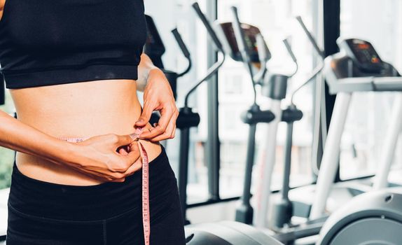 Beautiful woman using tape measuring waist, her is body slim after workout at fitness GYM