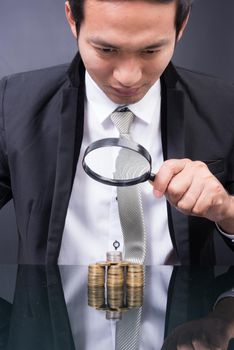 Businessman with magnifying glass looking With Stack Of Coins baht